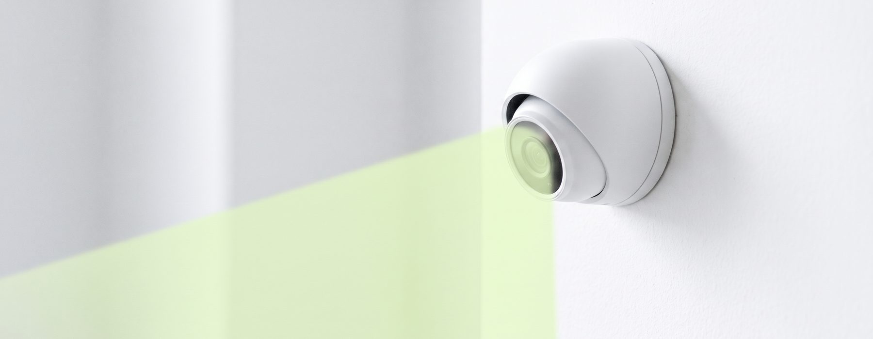 A wall-mounted dome camera casting a green detection cone